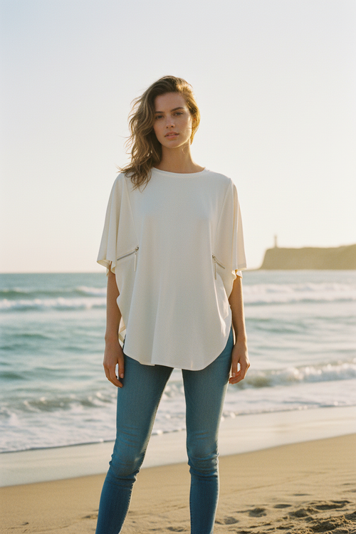 Female model wearing cream oversized blouse with side zippers and jeans at the seaside