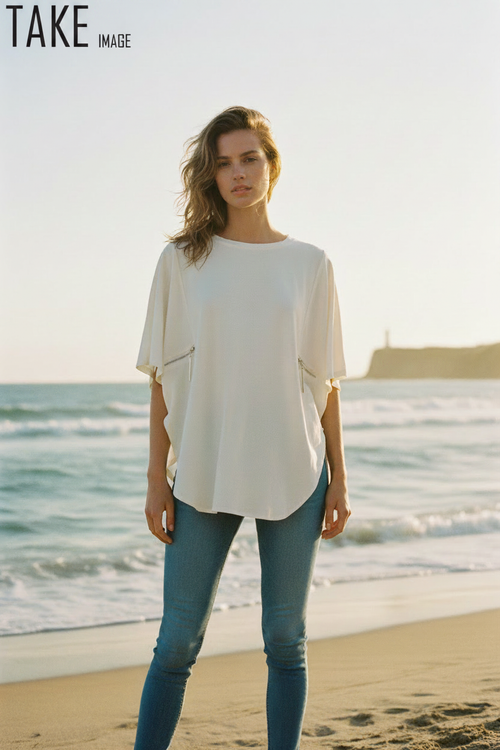 Female model wearing cream oversized blouse with side zippers and jeans at the seaside, with TAKE IMAGE logo